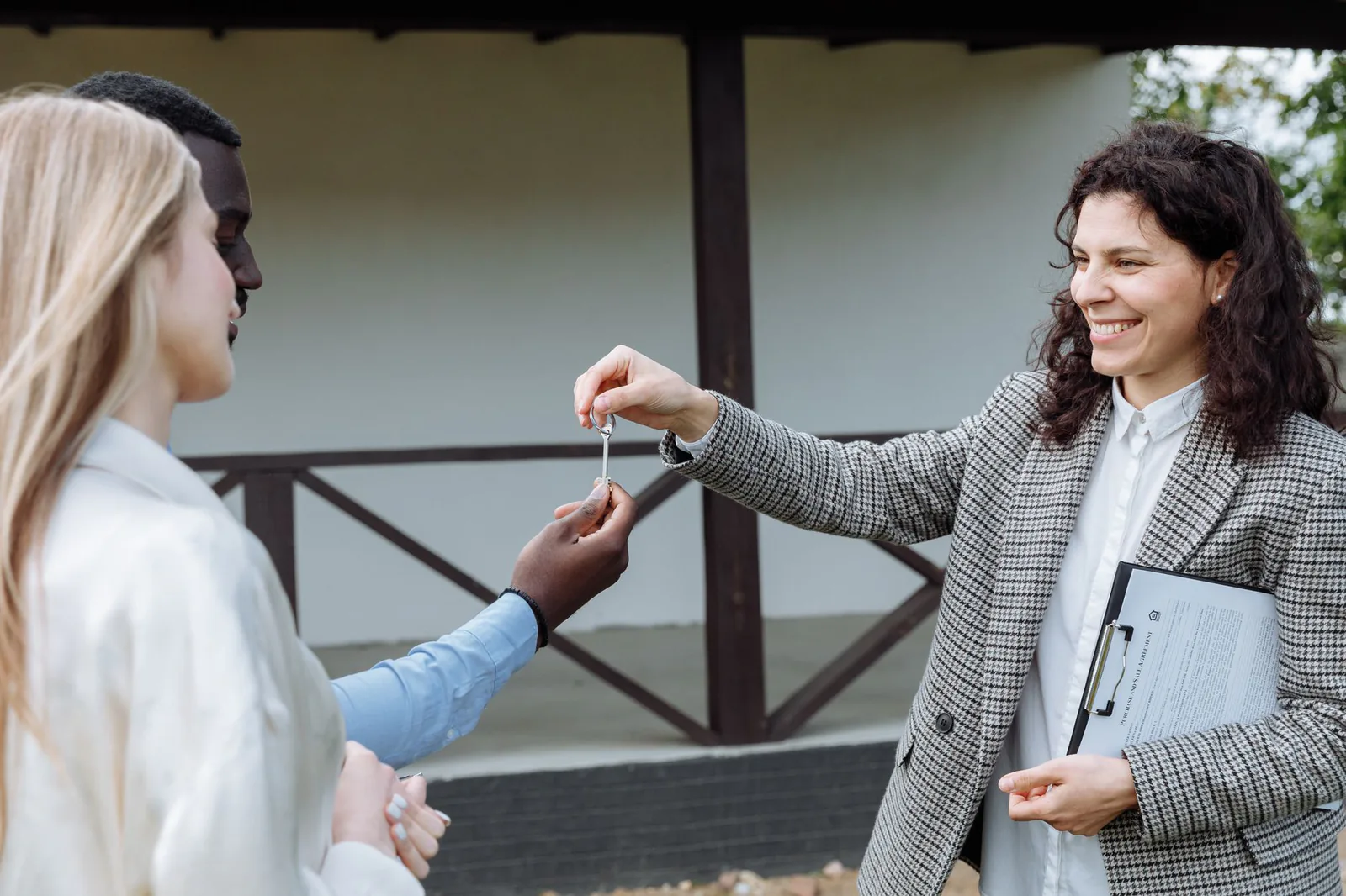 Realtor handing house keys to a happy couple in front of their new home