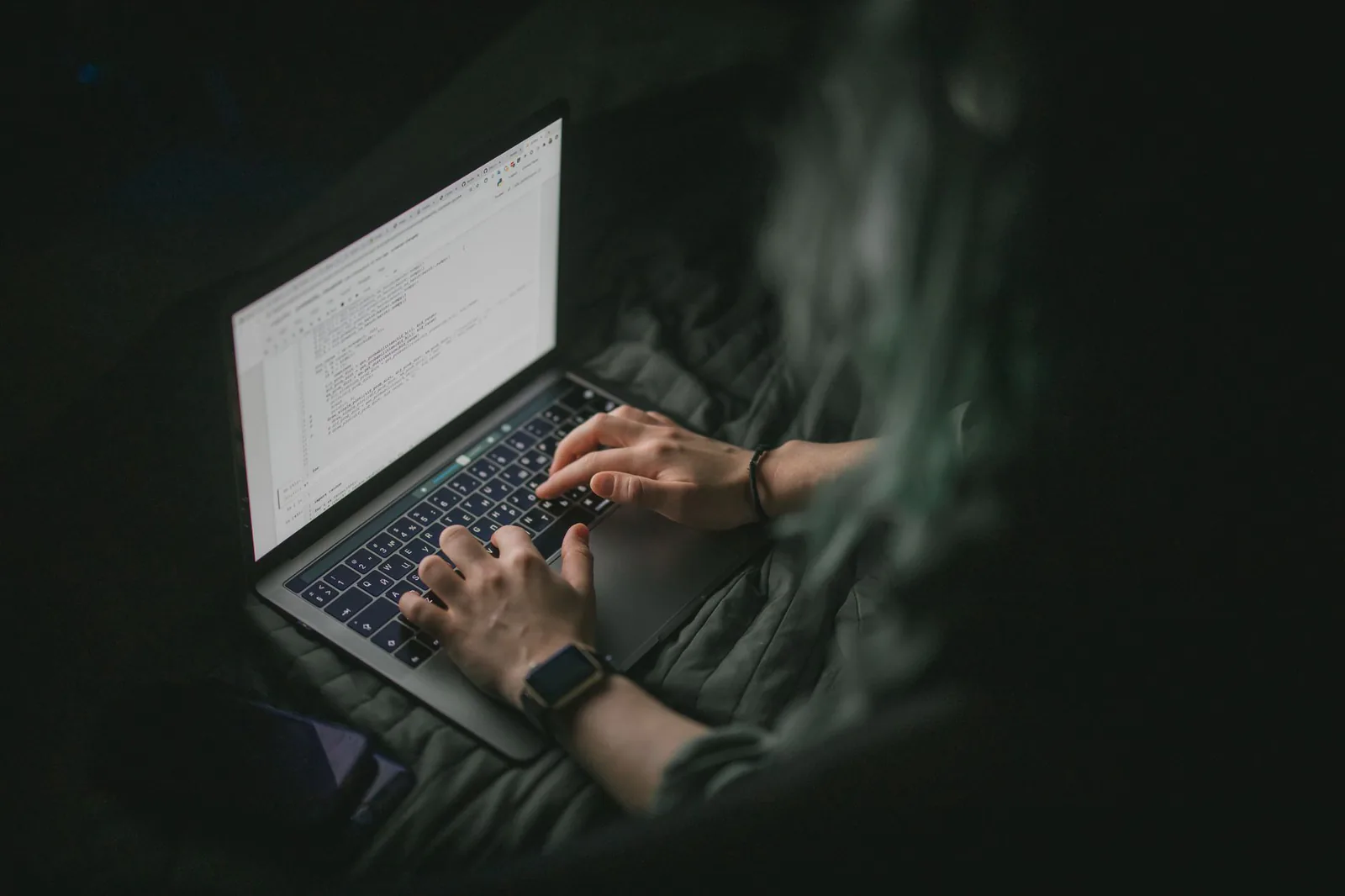 Developer typing code on a laptop in a dimly lit room